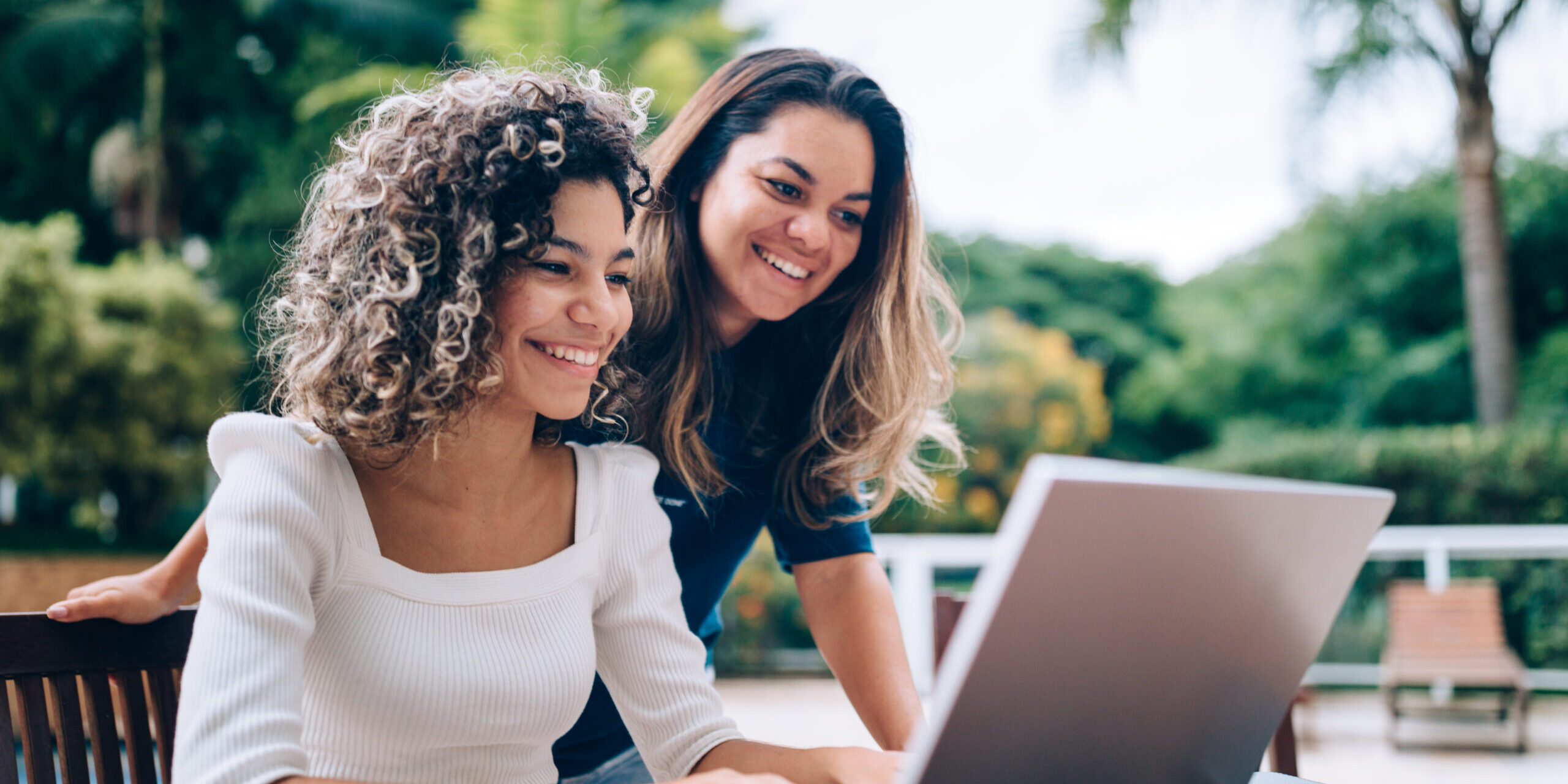Mother and daughter using laptop at swimming pool area